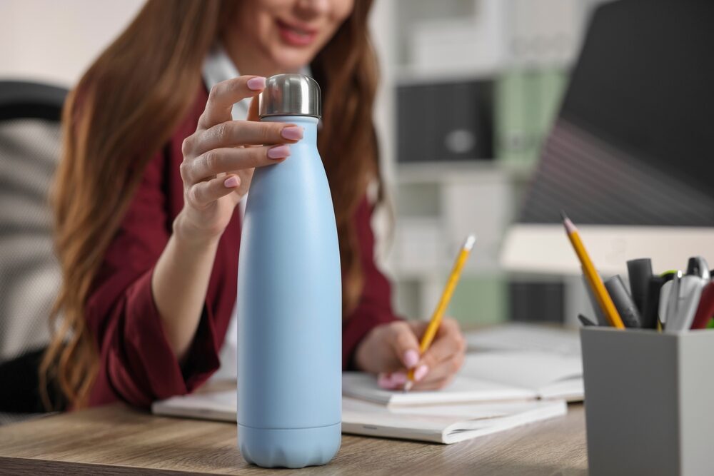 Woman,Holding,Thermos,Bottle,At,Workplace,,Closeup